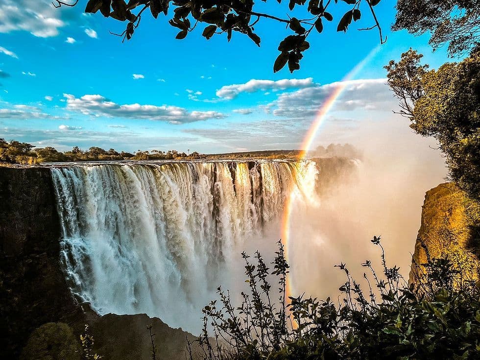 Victoria Falls waterfall with a rainbow cutting through the spray.